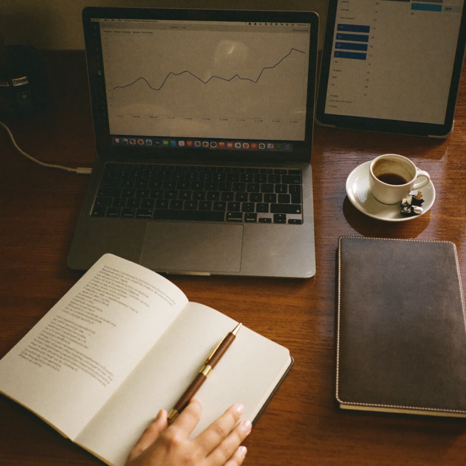 Schreibtisch-Detail mit Laptop, Tablet, Notizbuch und Espresso-Tasse